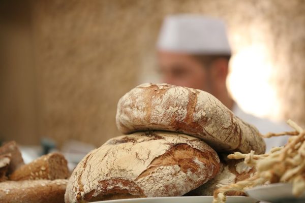 Fresh Italian breads stacked with a chef in the background